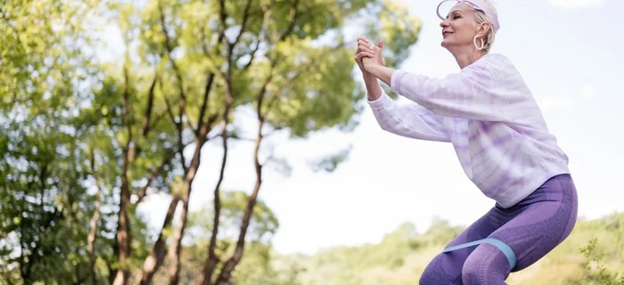 Older woman doing a lower-body strength exercise with a resistance band outdoors
